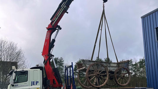 Crane lifting a carriage onto a truck for transport on a cloudy day.