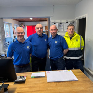 Four male colleagues smiling behind a reception desk.