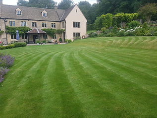 Perfectly striped lawn in front of a large stone country house and landscaped gardens