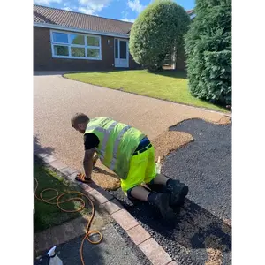 A worker in a high-visibility vest kneeling to hand-trowel a light brown aggregate driveway
