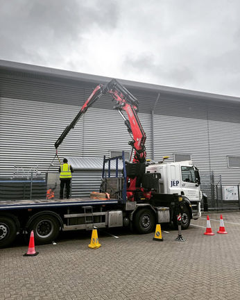 Crane truck lifting a load, with a worker and orange traffic cones present.
