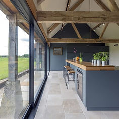 A modern kitchen with a large island and a full wall of glass doors opening to a field