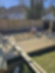 A person is kneeling on a partially constructed wooden deck in a backyard
