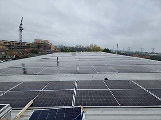 A large commercial roof with rows of installed solar panels and a crane in the background