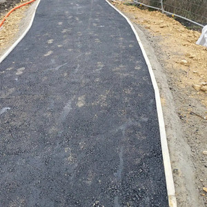 A new, winding black tarmac footpath with concrete kerbing, set into an earth embankment