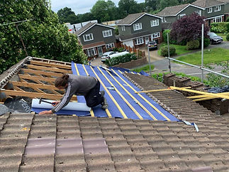 Roofer hammering new roofing battens over blue waterproof membrane during replacement