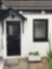 Black composite stable door beneath a canopy next to a black framed window on a white rendered house