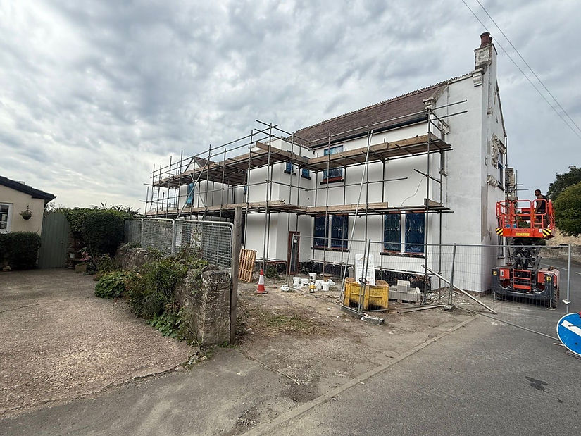Side of large house with scaffolding and white render visible behind framework