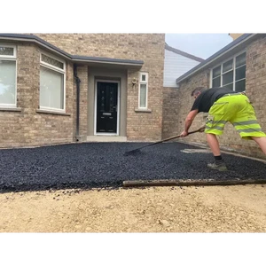 A worker in high-visibility shorts raking fresh black tarmac onto a driveway sub-base