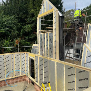 Construction worker on scaffolding builds new house, walls with framing and insulation.