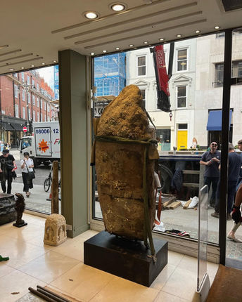 Large, textured sculpture in a storefront window with people and city view.
