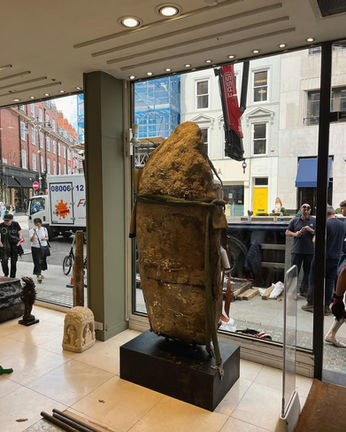 Large, textured sculpture in a storefront window with people and city view.