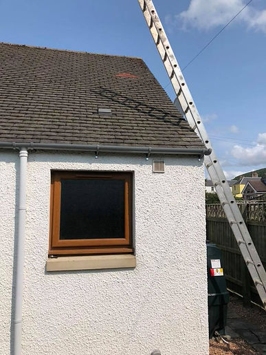 Upward view of newly installed black uPVC guttering and downpipes against a grey roughcast wall