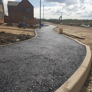 A new black tarmac footpath with concrete kerbing winding through a housing construction site
