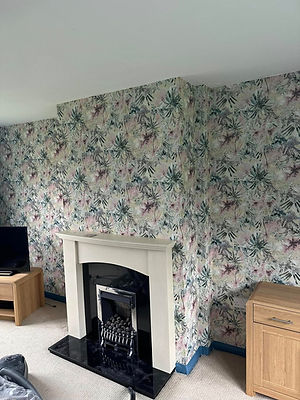 A living room decorated with colourful tropical leaf wallpaper and a classic white fireplace