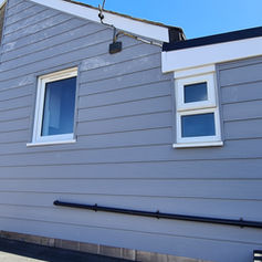 The side of a house with grey horizontal cladding and a small flat roof