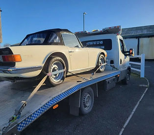 Classic car secured on a recovery truck being transported on a flatbed trailer