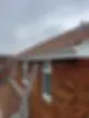 A silver ladder leaning against a brick house with a white gutter and red tiled roof