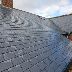 Newly tiled dark grey slate roof glistening with scaffolding and chimneys visible