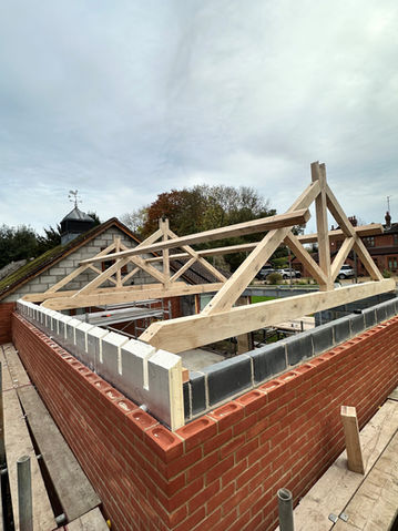 Wooden roof trusses under construction on brick walls against cloudy sky.