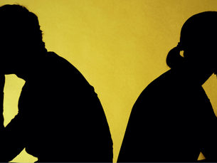 Silhouetted man and woman sitting back-to-back, lost in thought, against a bright yellow background. Mood is contemplative and distant.