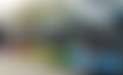 Colorful buses lined up in a row on a street, each with distinct branding. Trees and buildings are visible in the background.