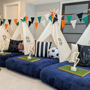 Game On kids’ sleepover theme with navy and white bedding, sports balls, green turf trays, and playful lighting.