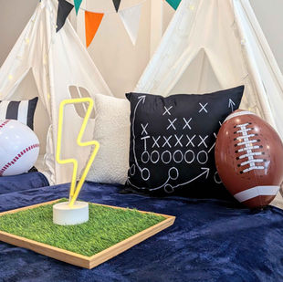Cozy sports-themed sleepover beds with navy blankets, turf-covered trays, lanterns, and sports ball party favors.