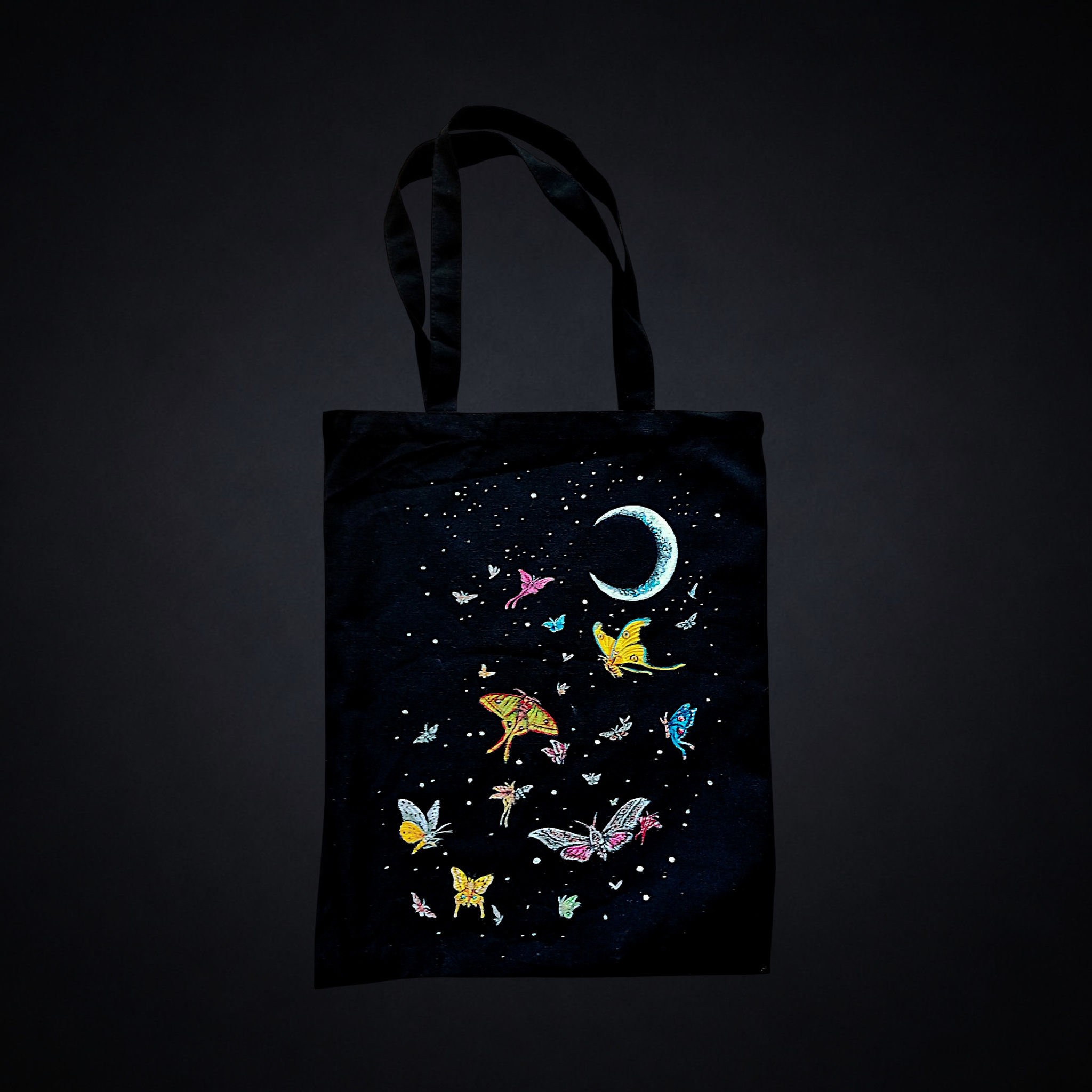 Noche de Polillas, tote bag negra única pintada a mano por Kuzen Saha con una luna creciente, polillas de colores y estrellas