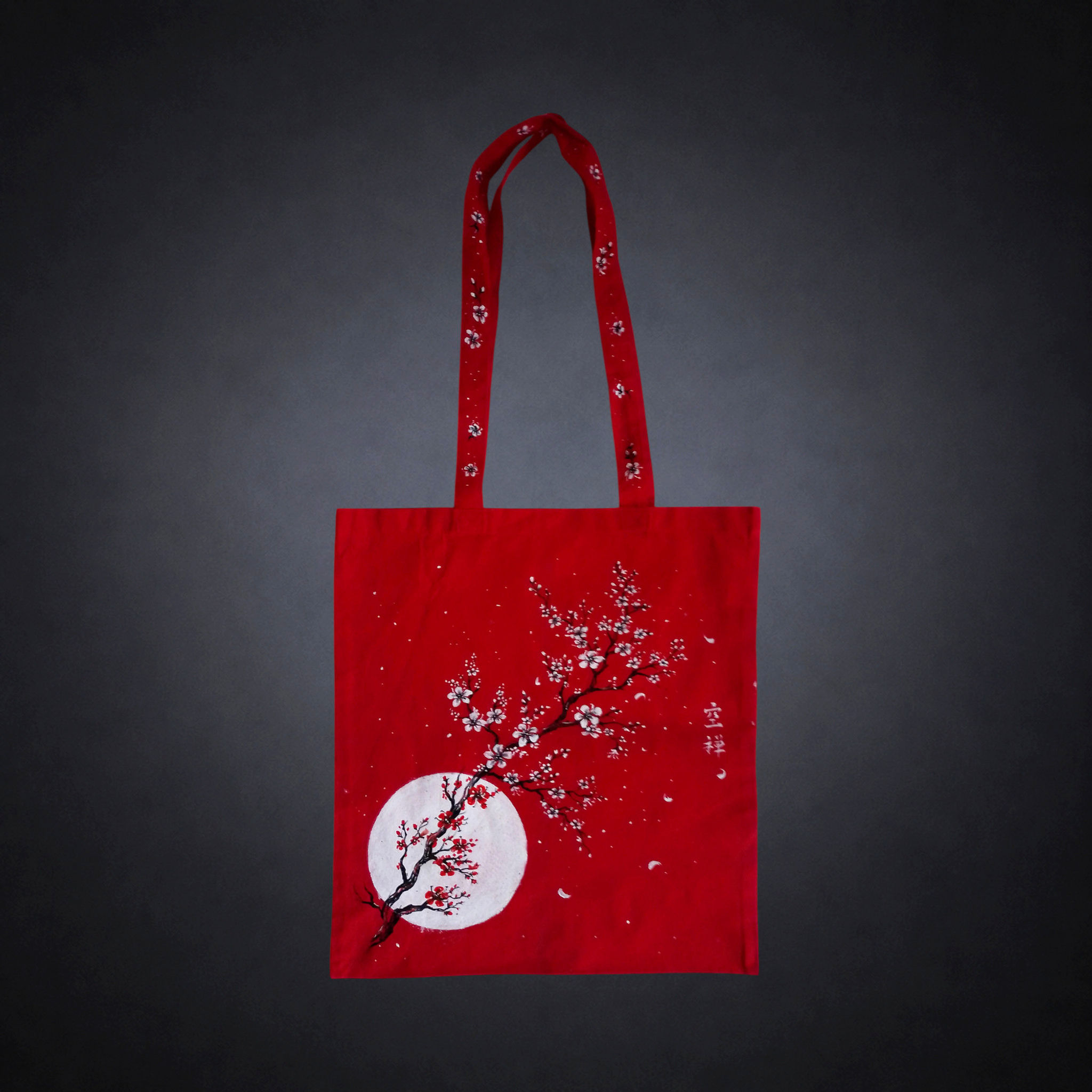 Luna de Cerezo, tote bag roja única pintada a mano por Kuzen Saha con una luna blanca y ramas de flores de cerezo.