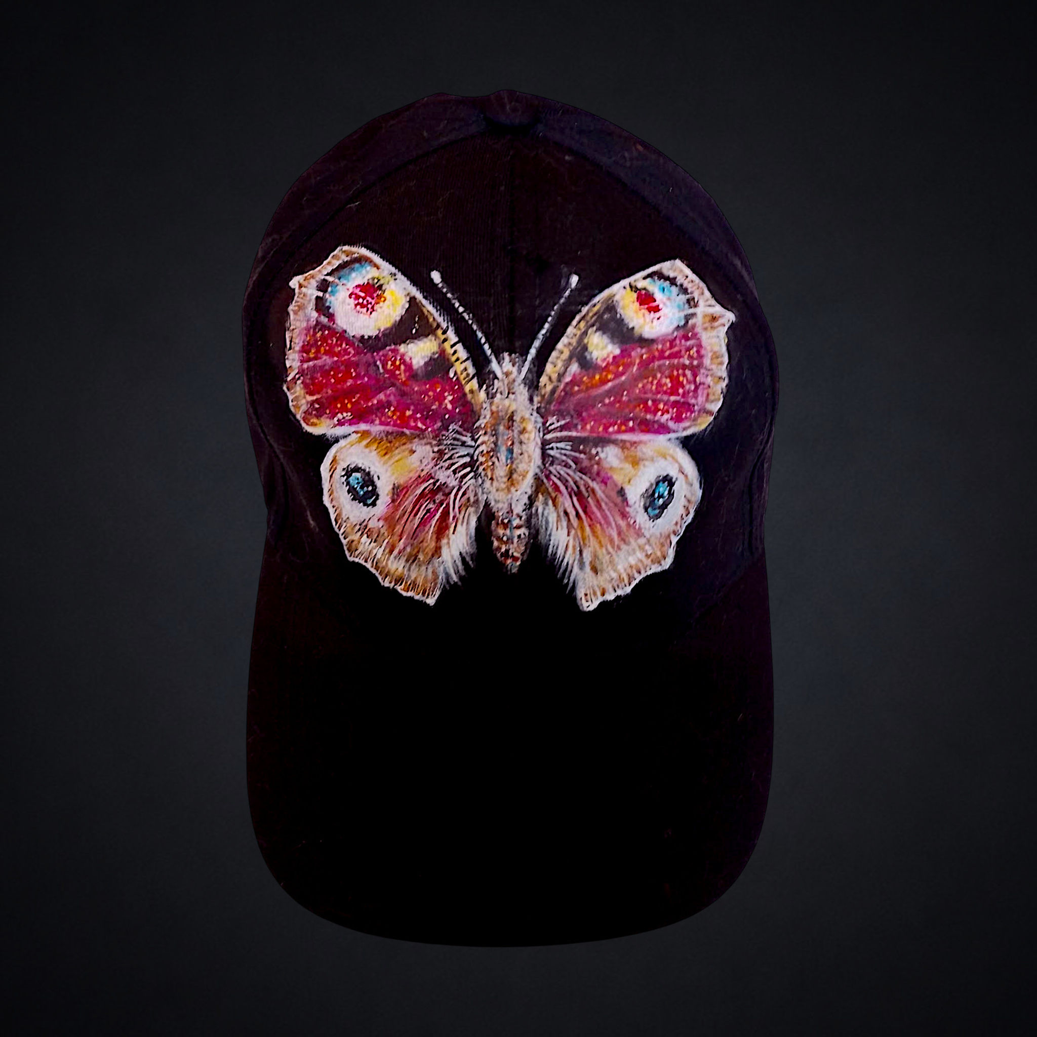 Aglais io, gorra negra única pintada a mano por Kuzen Saha con una mariposa pavo real de alas extendidas.
