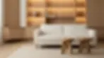 Interior design photography of a cozy, minimalist living room featuring a cream-colored sofa set against a backlit oak bookshelf. The scene evokes warmth and modern sophistication with its neutral tones.