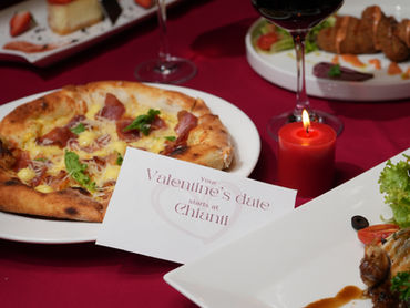 Pizza, wine glasses, and red candles on a table with a Valentine's message card. Romantic dinner setting on a red tablecloth.