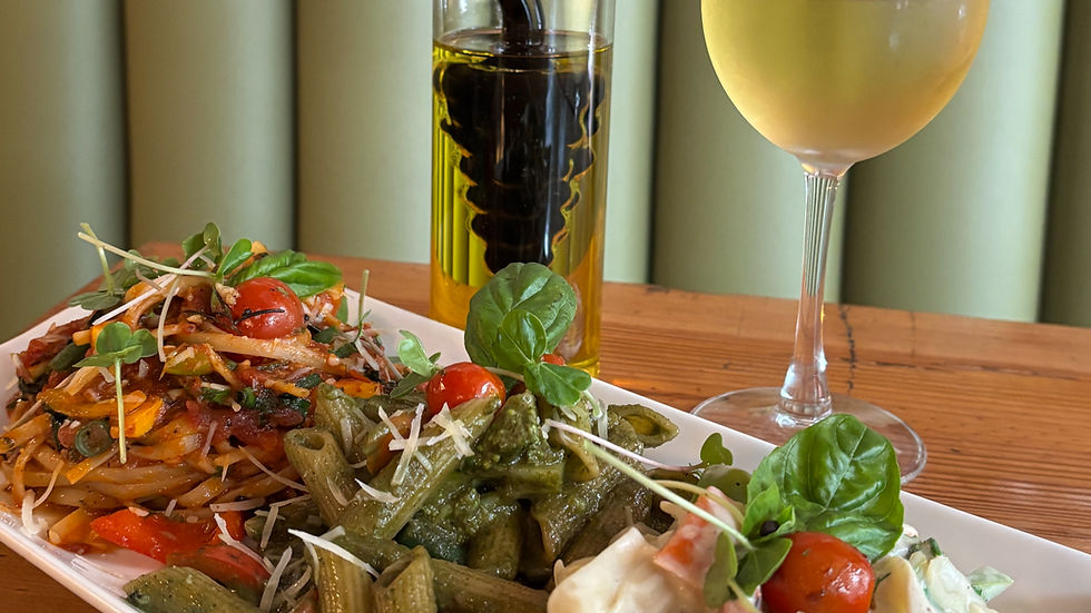 A plate of trio pasta with basil and cherry tomatoes, olive oil and vinegar bottle, and a glass of white wine on a wooden table, an limited time menu at Chianti Ristorante, Bengaluru