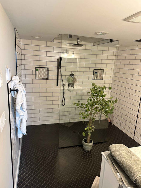 Floor to ceiling subway tile shower with black tile flooring and glass shower doors.