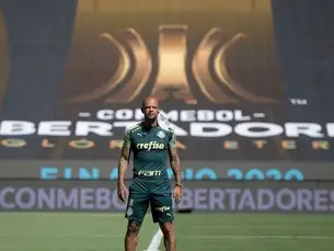 Jogador do Palmeiras em pé no gramado, com uniforme verde, diante de painel da final da Conmebol Libertadores.