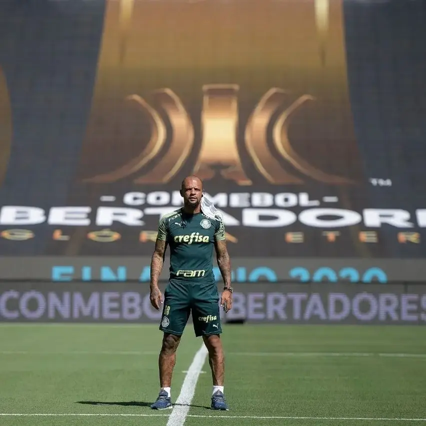 Jogador do Palmeiras em pé no gramado, com uniforme verde, diante de painel da final da Conmebol Libertadores.
