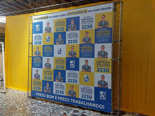 Banner amarelo e azul com foto de Delegado Fernando Veloso 2230 e PL, em ambiente coberto; frase Preso bom é preso trabalhando.