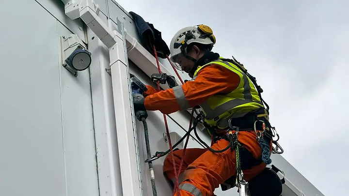 Rope access worker in orange coveralls and a high-visibility vest works on a white building facade