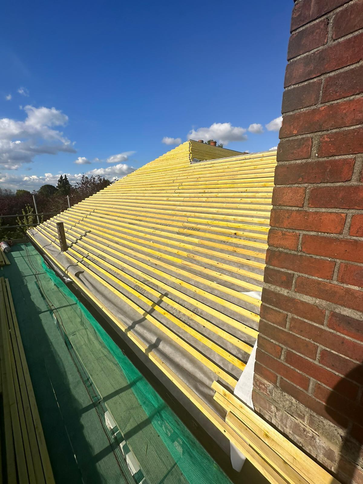 Roof batten installation beside brick chimney.