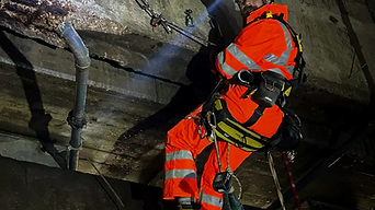 Rope access worker in orange safety gear inspects a concrete tunnel