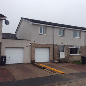 A two-story semi-detached house with a grey roof and white stone exterior.