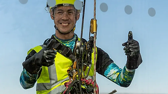 Smiling rope access worker in a yellow helmet and high-visibility vest gives a thumbs-up