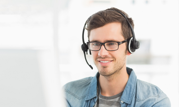 Smiling customer service representative with headset, glasses, and denim shirt assisting customers.