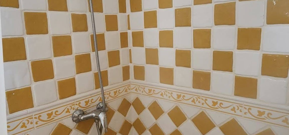Shower corner with beige and white patterned wall tiles, handheld showerhead, and tiled floor.