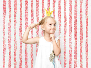a little girl with blonde hair wears a paper crown and smiles precociously