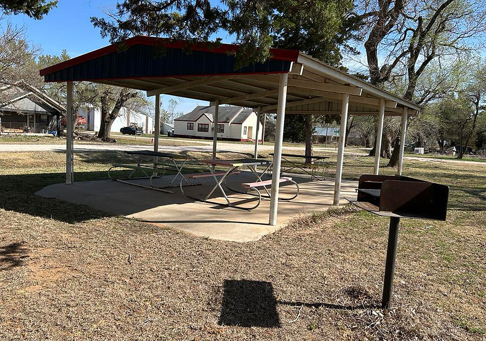 A covered shelter in Amorita Park covers three picnic tables. A barbecue grill sits on the outside of the shelter.