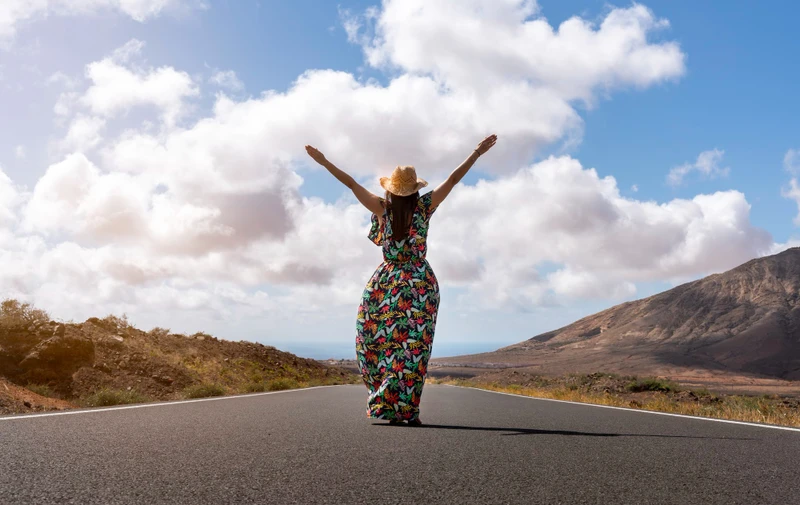 Woman on a deserted road in front of the sea raising her arms for the freedom