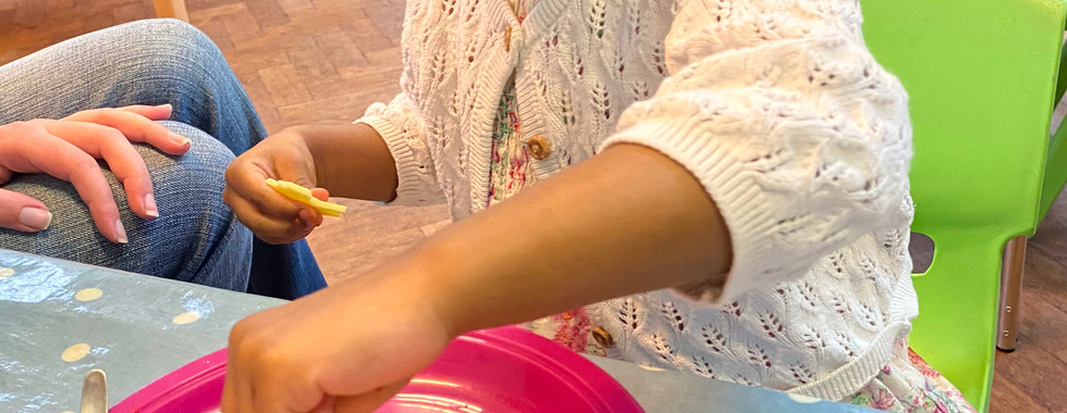 Young girl adding cheese and sweetcorn onto a crumpet pizza as part of cooking projects with toddlers at Shining Stars Nursery in Cardiff