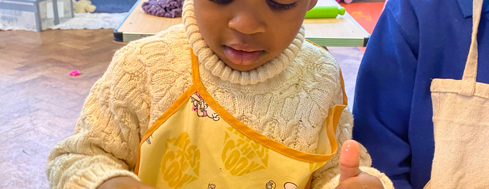 Young boy cracking egg for pancakes as part of cooking projects with toddlers at Shining Stars Nursery in Cardiff